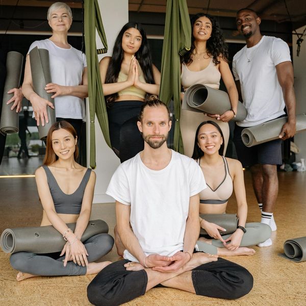 Group of diverse people sitting on yoga mats in a bright studio.
